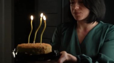 Pullu elbiseli bir kadın doğum günü pastasına mum üflüyor ve kutlamaya sıcaklık katıyor.