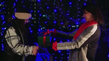 Sıcak kışlık elbiseli kadınlar gece şehrinde mavi ışıklarla çevrili hediyelerini değiş tokuş ederler. Arkadaşlıkları ve tatil buluşmalarını kutlamak için mükemmel.