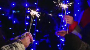 Dışarıdaki neşeli bir grup kadın, arka plandaki mavi çelenk ışıklarına bakarak, Noel gecesi şehrin coşkusunu gösteriyorlar.