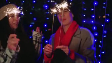 Yeni yıl arifesinde mavi ışıklara karşı maytap tutan neşeli üç kadın. Yeni yıl kutlamaları için neşeli ve parlak bir atmosfer.