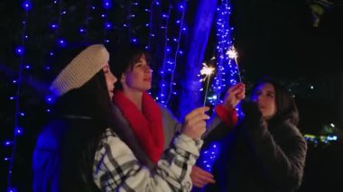 Parıldayan mavi ışıklar altında parıldayan kıvılcımlarla gecenin tadını çıkaran üç kadın, her biri eşsiz kıyafetler giymiş. Şenlikli anları ve dostluğu yakalamak için mükemmel.