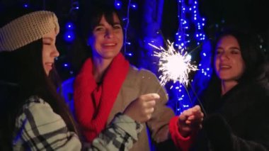 Parıldayan mavi ışıklar altında parıldayan kıvılcımlarla gecenin tadını çıkaran üç kadın, her biri eşsiz kıyafetler giymiş. Şenlikli anları ve dostluğu yakalamak için mükemmel.