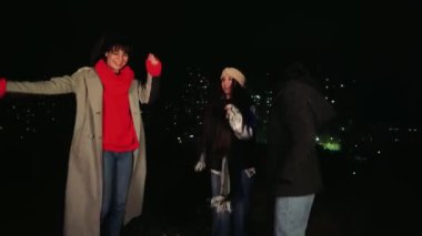 Üç arkadaş gece şehirde gezmek için toplanıyor, ışıklarla aydınlatılıyor, açık havanın tadını çıkarıyorlar. Kış tatili ve arkadaşlık için mükemmel.