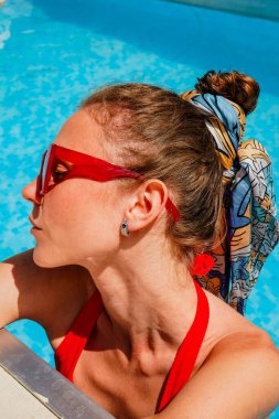 Fashionable woman in red swimwear relaxing in a swimming pool, exuding summer vibes. Poolside portrait of a woman in a red bikini and bold sunglasses, enjoying the sunny day clipart