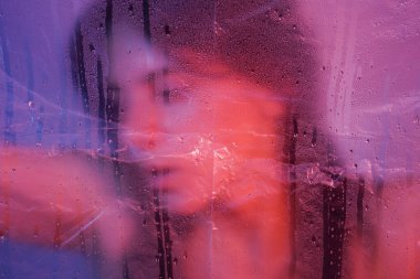 Şeffaf plastik folyonun arkasında elbise giymiş çekici, uzun saçlı bir kız. Mor ışıklandırma. Yüksek kalite fotoğraf