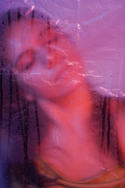 Makyajlı beyaz bir kızın portresi ciddi bir ifadeyle plastik bir katmanla yana bakıyor. Sanatsal fotoğrafçılık. Yatay çekim. Yüksek kalite fotoğraf