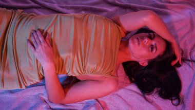 Yerde yatan, dişlek gülüşlü, elbise giymiş genç bir kızın portresi.