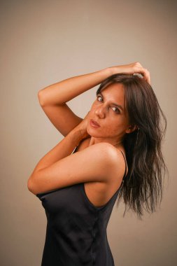 Uzun düz saçlı ve doğal makyajlı genç bir kadın stüdyoda poz veriyor. Bir kadın gri arka planda zarif bir poz alır, zarafet ve çekicilik.