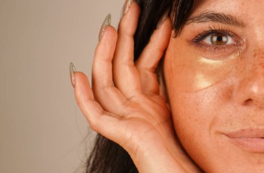 Doğal makyajlı güzel bir kadın gözünün altındaki altın lekeyi temizler. Kozmetik ve cilt bakımı. Işık arkaplanında izole