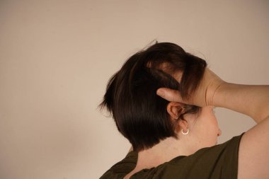 Başı ağrıyan bir kadın başını tutar ve sırtını gri duvara döner.