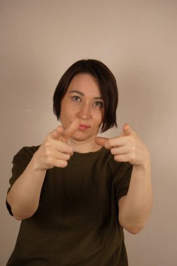 Kadın doğrudan kameraya bakar ve işaret parmaklarıyla baktığı yeri gösterir. Kapatın. İzole edilmiş gri bir arkaplanda