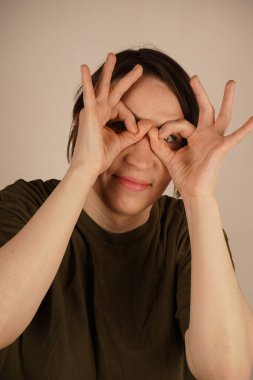 Beyaz stüdyo arka planında güzel bir jest sergileyen ve elleriyle dürbün yapan çekici genç kadının portresini kapat.