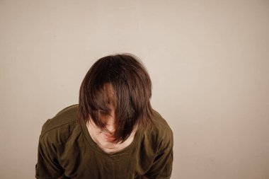 Bej renkli stüdyo arka planında kısa düz saçlarına bakan üzgün genç bir bayan. Dağınık saç stilinden memnun olmayan, hayal kırıklığına uğramış milenyum kadını. Kırık uçlar için kuaför salonuna gitmesi gerekiyor.