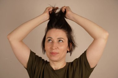 Neşeli esmer genç kadın elinde tutuyor kısa saçlarını bej arka planda izole edilmiş, maske tedavisi, diyet düzeltmesi, merhem, vitamin, fotokopi alanı.