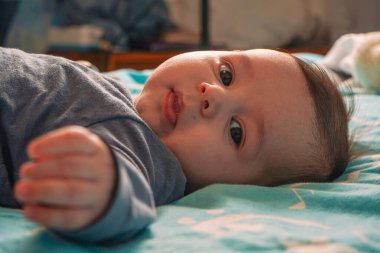 Bedenli, sevimli, mutlu çocuk sınıftaki karyolada şiltenin üstünde yatıyor. Yukarıdan bak. Bebek oyun oynuyor. Kapat.