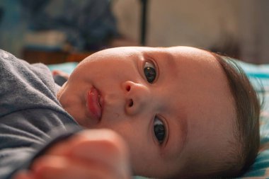 Yatağında, sırt üstü, gri pijamalarıyla, bulutların arasında kollarını kaldırmış, sağlıklı bir şekilde uyuyan bir bebek.