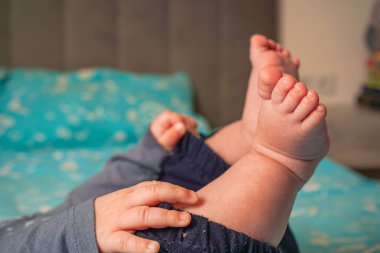 Relaxed yet playful, the child in dark pants and a gray top stretches their legs skyward while lying on their back on a vivid blue canvas clipart