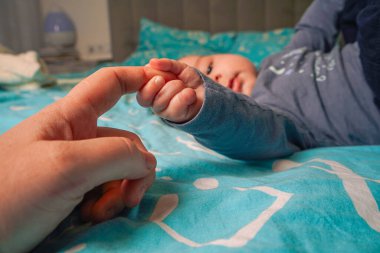 Hareketsiz bir poz veren gri kazaklı ve siyah pantolonlu çocuk sırtüstü uzanmış, koyu mavi arka planda mükemmel bir şekilde duruyor.