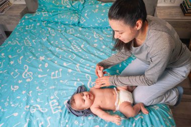 Genç bir anne, yumuşak mavi bir battaniyeye oturur ve kontrolsüz bir şekilde gülümseyen bebeğine hafifçe gülümser.