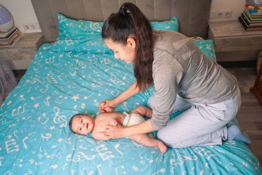 Bir anne, çocuğunun bacaklarına evde bir karyolada masaj yapar. Annem evde çocukla oynuyor.