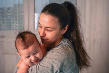 Bir anne mavi kaplı bir yatağın kenarına oturur, bezi bezlenmiş oğlunu kollarına alır akşam karanlığının ışıltısı pencerenin arkasından süzülürken.