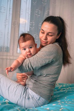 Anne, oğlunun sırtını nazikçe okşar. Sevgi dolu bakışları ona sabittir. Yumuşakça cıvıldar, rahatlatıcı dokunuşundan zevk alır.