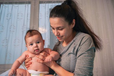Bir anne mavi kaplı bir yatağın kenarına oturur, bezi bezlenmiş oğlunu kollarına alır akşam karanlığının ışıltısı pencerenin arkasından süzülürken.
