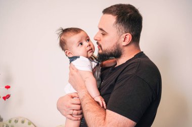 Bir eliyle bebekleri desteklerken, diğer eliyle de babaların hareketleri özen ve güven gösteriyor.