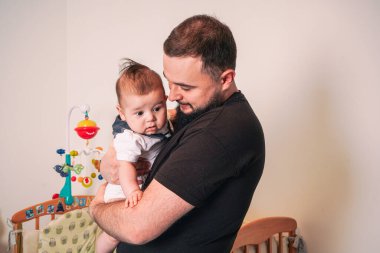 Şaşırmış yeni doğmuş bebek babasının kollarında bej rengi izole bir arka plan, evde küçük bir bebek, yakın plan.