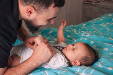 Sevgi dolu bir bakışla baba, çocuğunun yumuşak mavi yüzeyde huzur içinde dinlenmesine hayran.