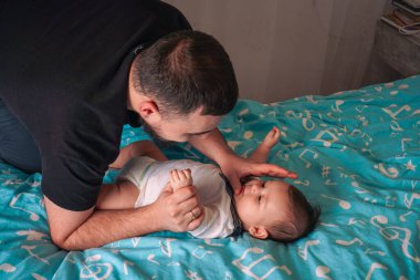 Bir baba bebeğinin üzerine eğilir ve içtenlikle dolu mavi battaniyede özel bir bağ yaratır.