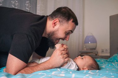 Bir babanın bebeğiyle sıcak mavi bir battaniye üzerinde nazikçe etkileşime girdiği hassas bir an başlıyor.