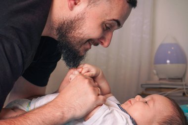 Gururlu bir baba yakına eğilir, elleri usulca bebeğe dokunur, koşulsuz sevgi gösterir.