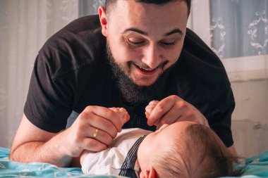 Beyaz tulumlu bebek kıkırdıyor, bu özel bağı bağlamak için eğilen babaya sıcak bir gülümseme getiriyor.