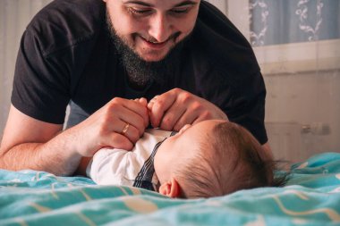 Baba elini bebeğin yanına koyar, yumuşak mavi yüzeyde sevgi ve güven sahnesi yaratır.