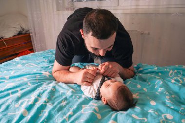 Yakından eğilirken, baba nazikçe bebeğinin küçük parmaklarına dokunur, mavi battaniyedeki sakin anın tadını çıkarır.