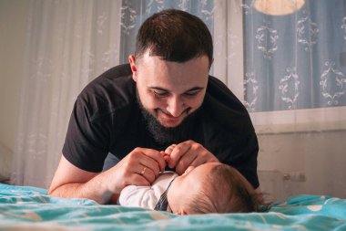 Bebeğin beyaz tulumu mavi battaniyeye karşı koyuyor, babaların sevgi dolu bakışlarını mükemmel çerçeveliyor.