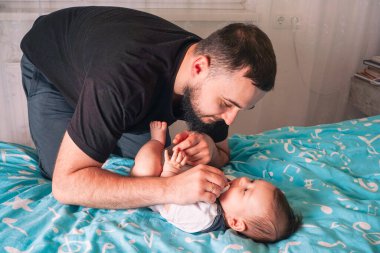 Bir baba bebeğinin üzerine eğilir, elleri nazikçe yakınına yerleştirilir, sıcaklığın ve özenin bir resmini yaratır.