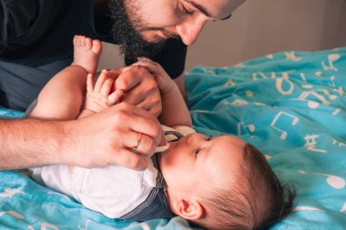 Bebek mavi battaniyenin üzerinde huzur içinde yatıyor, babasının koruyucu bakışlarının güvenliğinin tadını çıkarıyor.
