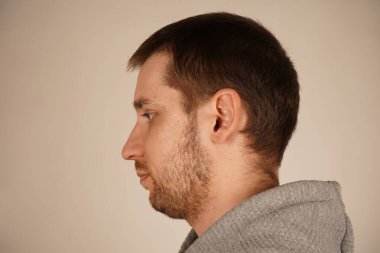 Yan taraftan gri kapüşonlu bir adamın yakın çekim görüntüsü. Onun kısa bir saç kesimi ve koyu renk saçlarında açık renk sakalı var. Onun sakin ifadesi rahat bir görünüm katıyor.