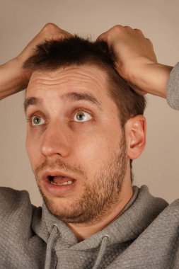 Elleri saçının üzerinde olan bir adam, yaygın bir jest, zihinsel bir aşırı yüklenme yaşıyor. Yüzünde hayal kırıklığı ya da endişe var. Görüntü yoğun düşüncelere ve strese verdiği tepkiyi vurguluyor.