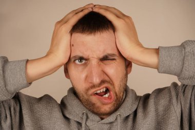 Bir adam iki elini de kafasında tutar. Stres ya da zihinsel gerilimi gösteren bir jest. Yüz ifadesi düşüncelerinin ağırlığını yansıtıyor. Görüntü, baskı ve endişe hissini yakalar.