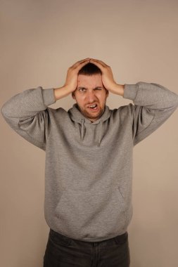 Bir adam iki elini de kafasında tutar. Stres ya da zihinsel gerilimi gösteren bir jest. Yüz ifadesi düşüncelerinin ağırlığını yansıtıyor. Görüntü, baskı ve endişe hissini yakalar.