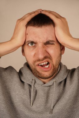 Bir adam iki elini de kafasında tutar. Stres ya da zihinsel gerilimi gösteren bir jest. Yüz ifadesi düşüncelerinin ağırlığını yansıtıyor. Görüntü, baskı ve endişe hissini yakalar.