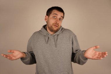 Elleri dışa doğru uzanmış, kafası karışmış bir adam omuz silkiyor. Açık avuçlar, onun durum hakkındaki anlayışsızlığını simgeliyor. Vücut dili belirsizliği ve merakı yansıtıyor.