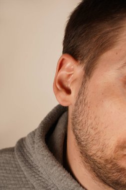 Bir adamın kulağının doğal çizgilerini ve deri dokusunu gösteren yakın çekimi. Görüntü basitliği ve detaylara dikkati vurgular. İnsan anatomisinin güzelliğini vurgulayan minimalist bir portre.