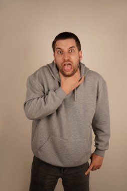 Bir adam boğazını eliyle kavrıyor, ağzı sonuna kadar açık sanki boğuluyormuş ya da öksürüyormuş gibi. Yüzündeki rahatsızlık, nefes almakta güçlük çekerken ya da öksürürken o anın aciliyetini gösteriyor.