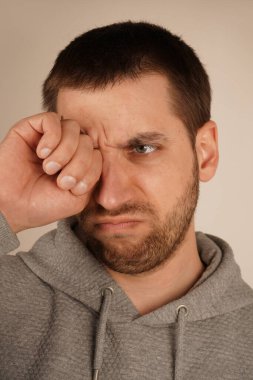 Uykulu genç adam yumruğuyla gözünü ovuşturur, yorgunluğu iletir. Uyanmaya ya da kendini rahatlatmaya çalışırken ifadesi yorgunluk gösteriyor. Jest, uyanık kalma mücadelesini yakalar.