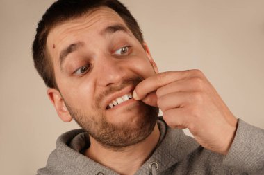 Genç bir adam dikkatlice dişlerinden bir şey çıkarır. Onun odaklanmış ifadesi bu hassas eylemde ayrıntılara dikkat çekiyor. Görüntü onun kesin hareketini yakalar.