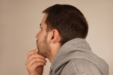 Bir adam düşünceli bir şekilde elini çenesinin üzerine koyar, derin düşüncelere dalmış bir şekilde görünür. Onun ciddi ifadesi derin bir düşünceyi yansıtır. Jest odak ve içgözlem öneriyor.